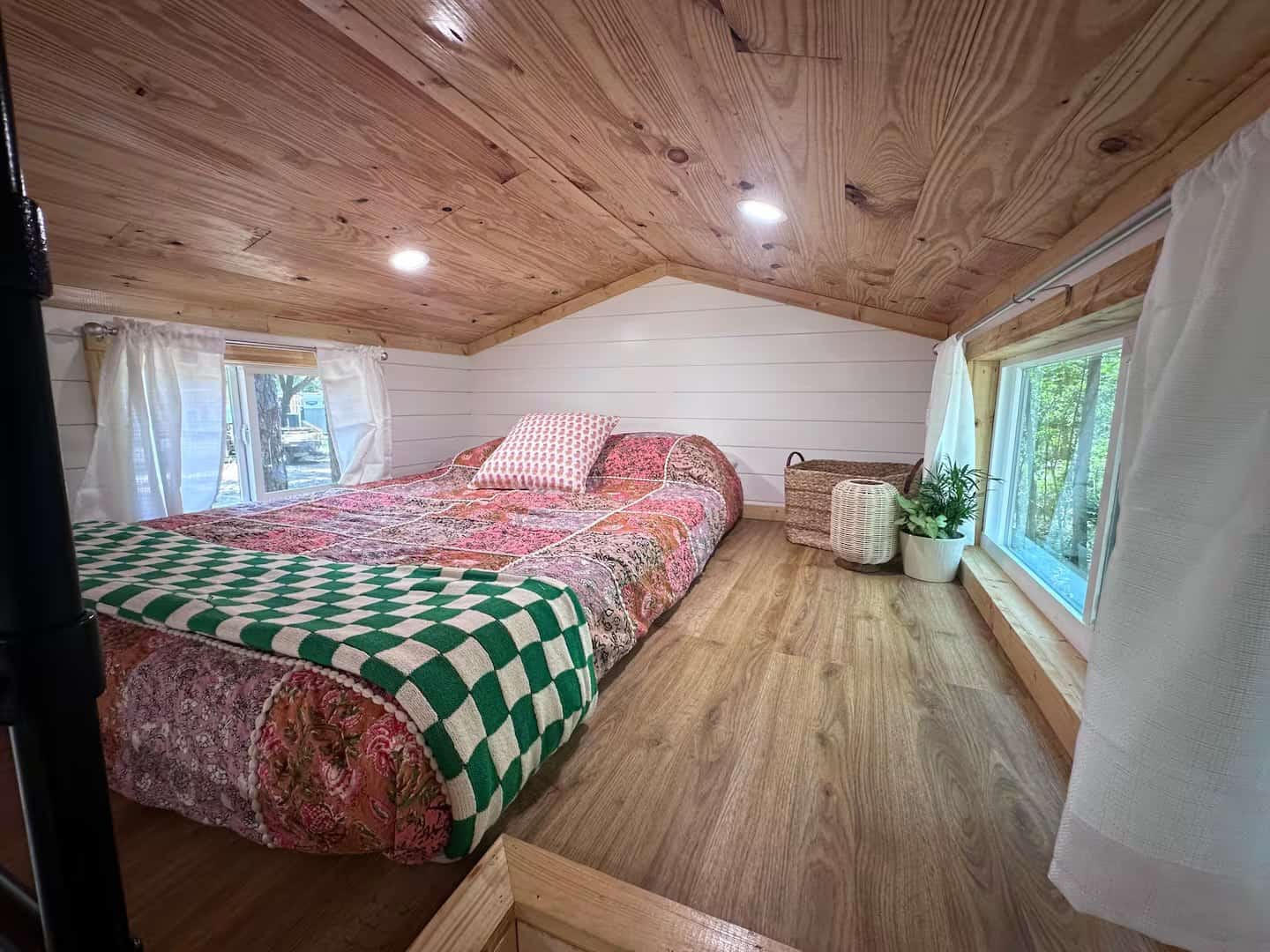 Sleeping loft in the Rasa tiny home with a full bed, pine ceiling, and bright windows