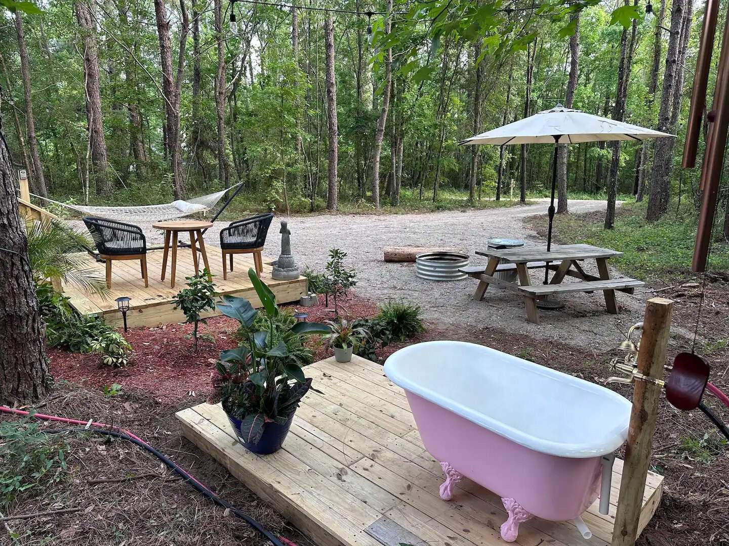 Pink outdoor clawfoot soaking tub on the deck at the Rasa tiny home, with a hammock and fire pit beyond