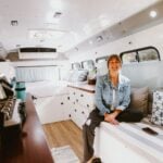 Interior of a tiny bus with a woman sitting on a built-in bench, showcasing compact living space.