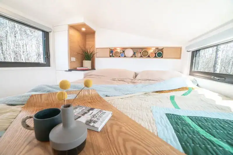 Interior of a tiny house with a cozy bed, large windows, and minimalist decor in Alberta, Canada.