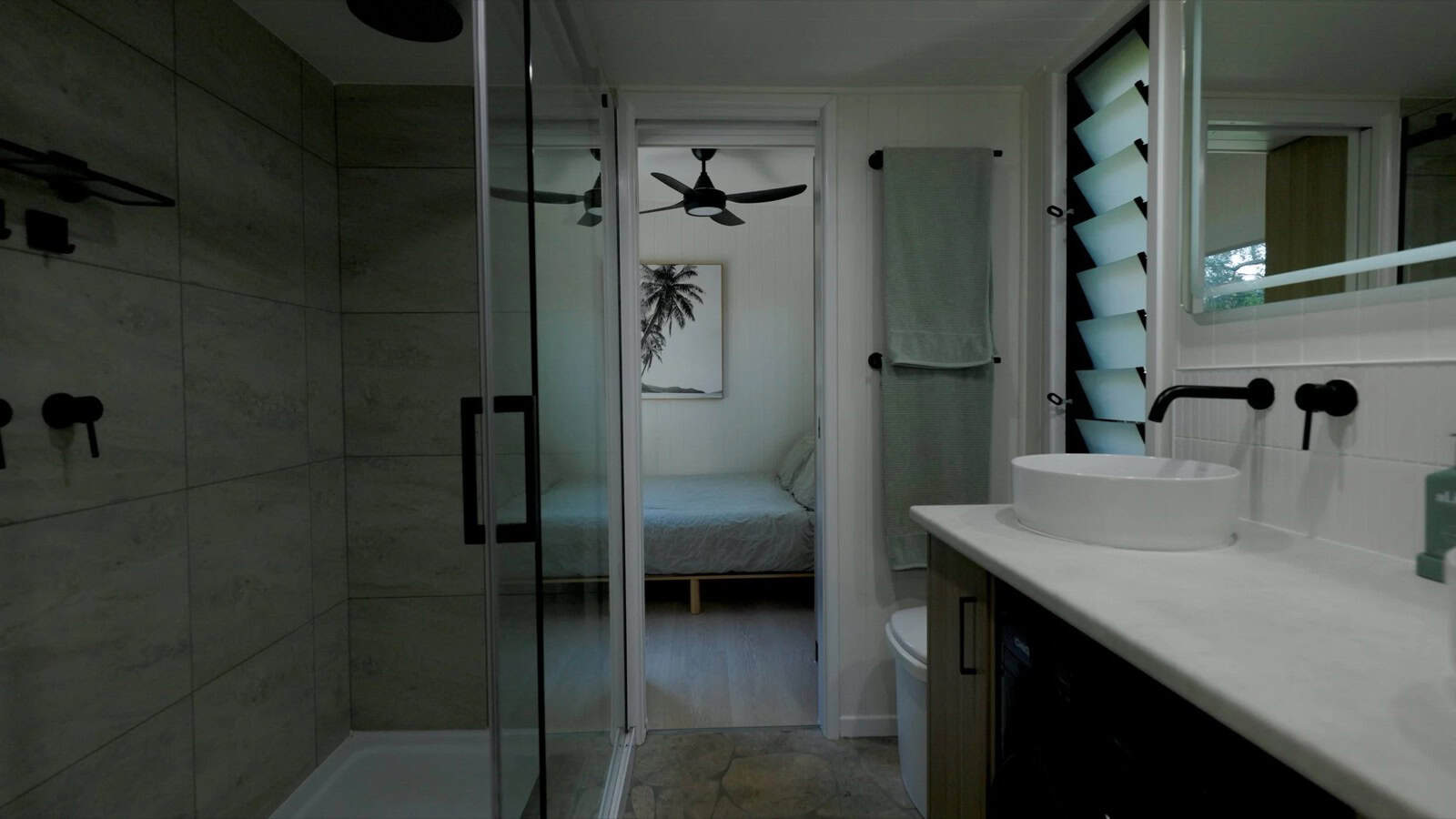 The Burleigh 9.6 bathroom with a glass-enclosed double shower in stone-look tile, a stone-topped vanity with a vessel sink, and the bedroom visible through the doorway