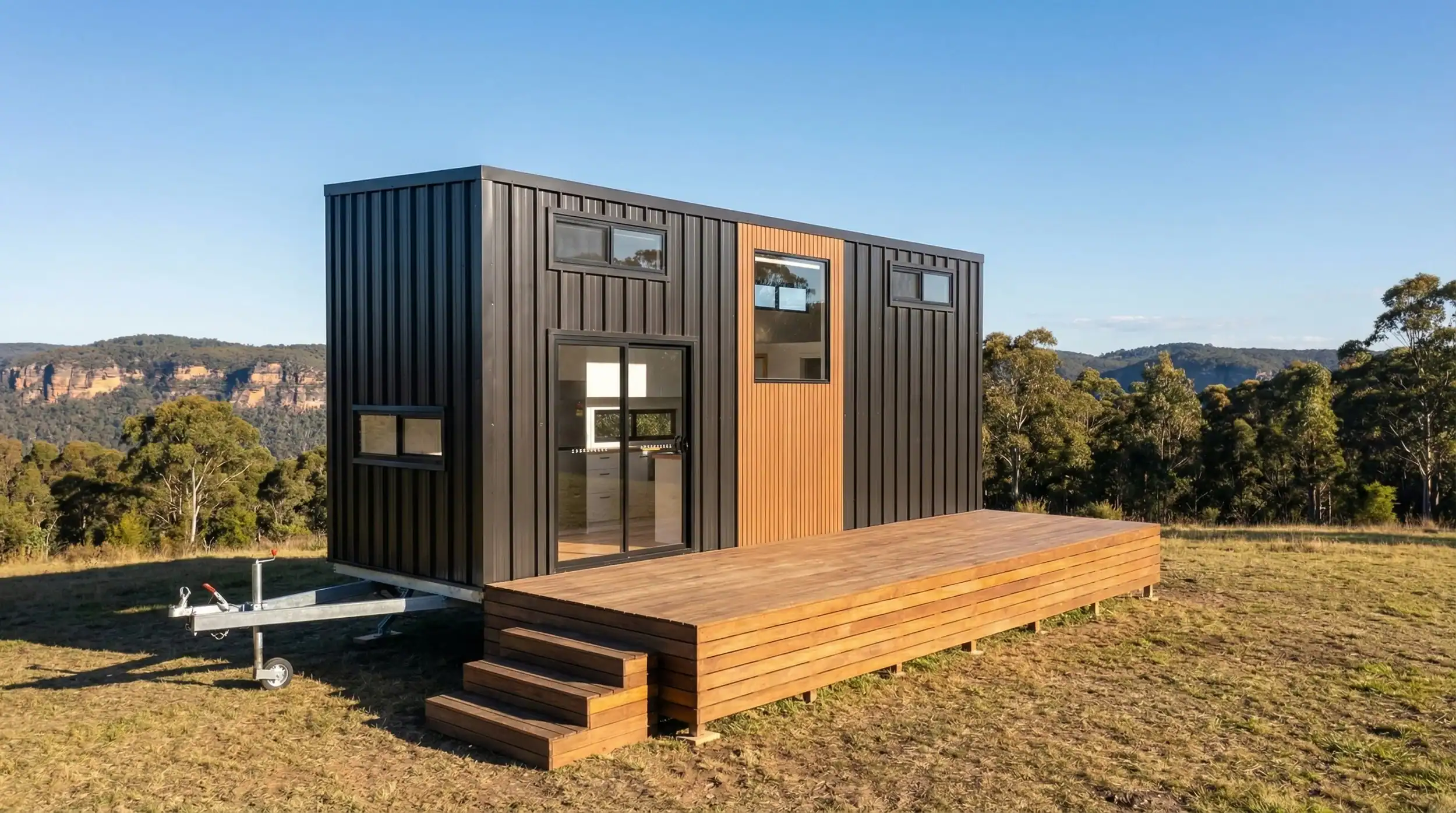 The Removed Byron Bay modern tiny house with dark cladding, timber entry, and a large deck set against a mountain backdrop