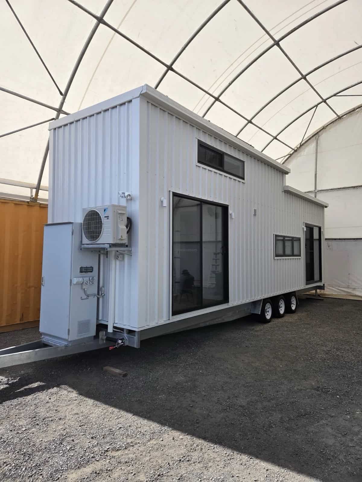 The Cabarita by Removed Tiny Homes, a white-clad tiny house on a triple-axle trailer with a raised loft and large sliding glass doors