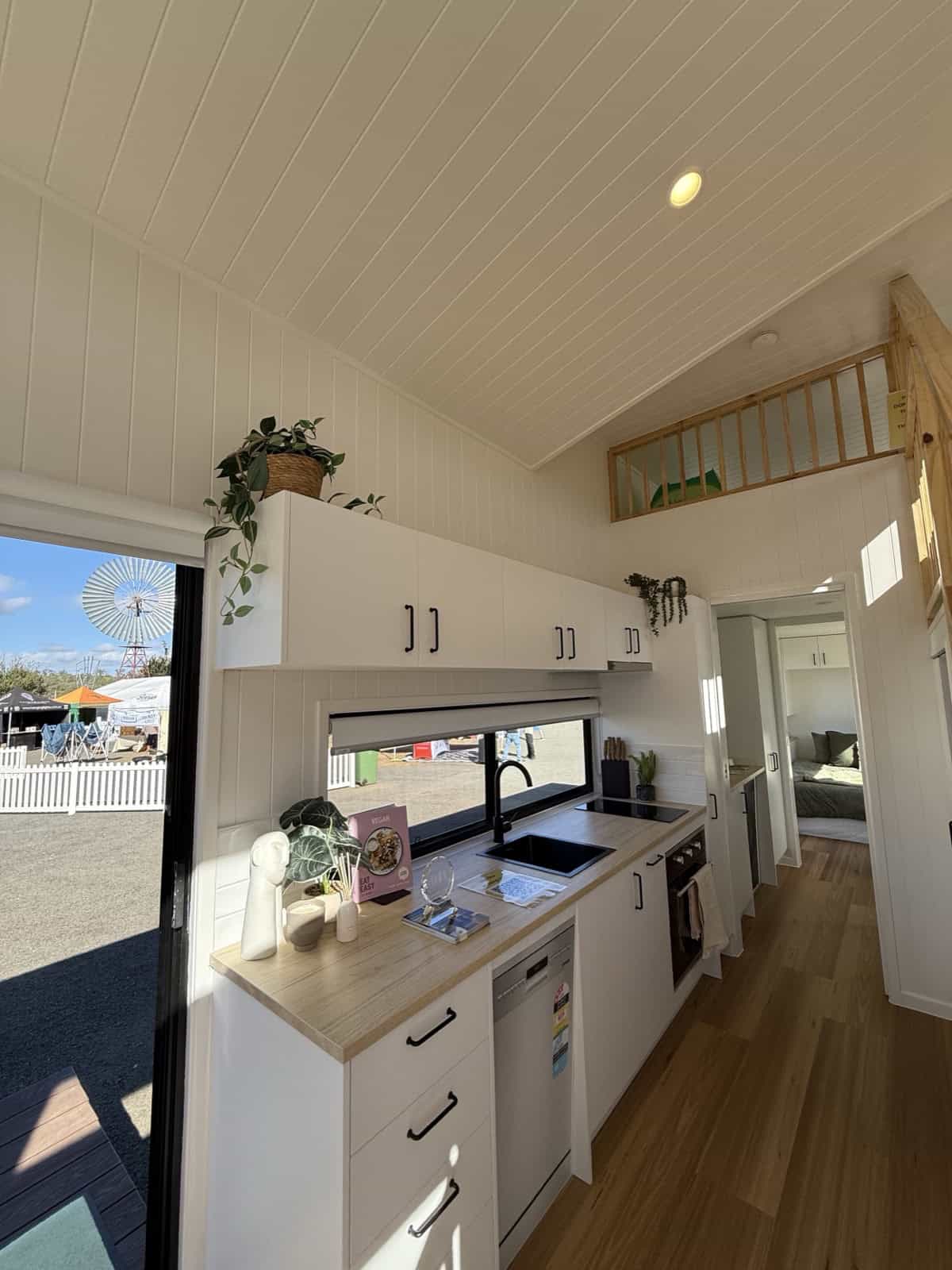 The Cabarita kitchen with white cabinetry, a timber benchtop, black sink and tap, induction cooktop, and a picture window over the sink
