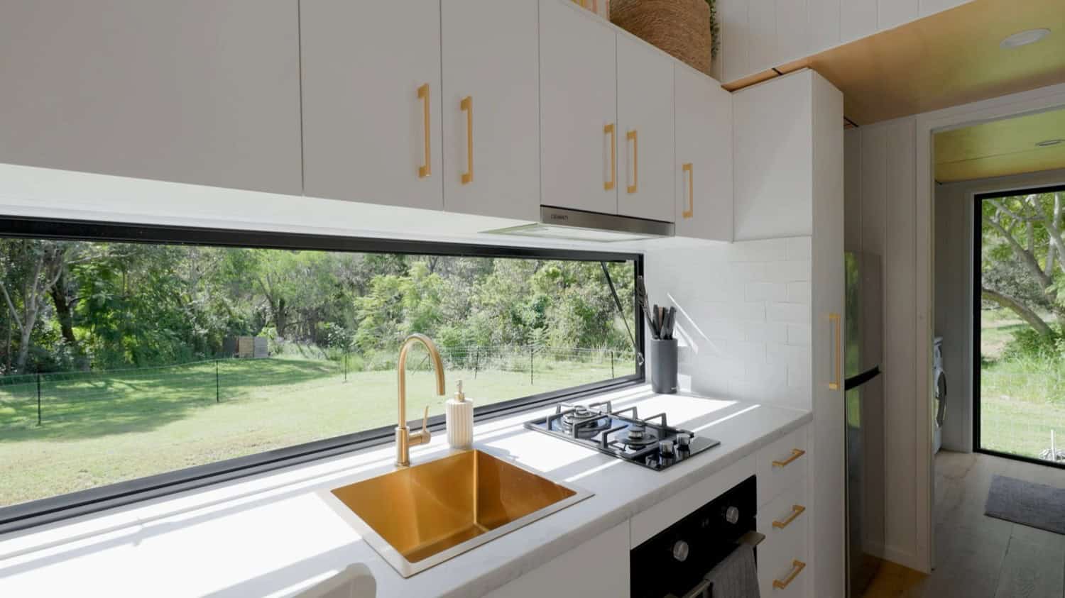 A detail of the Coolangatta kitchen with a brass sink and gooseneck tap, white stone benchtop, subway-tile splashback, gas cooktop, and under-bench oven
