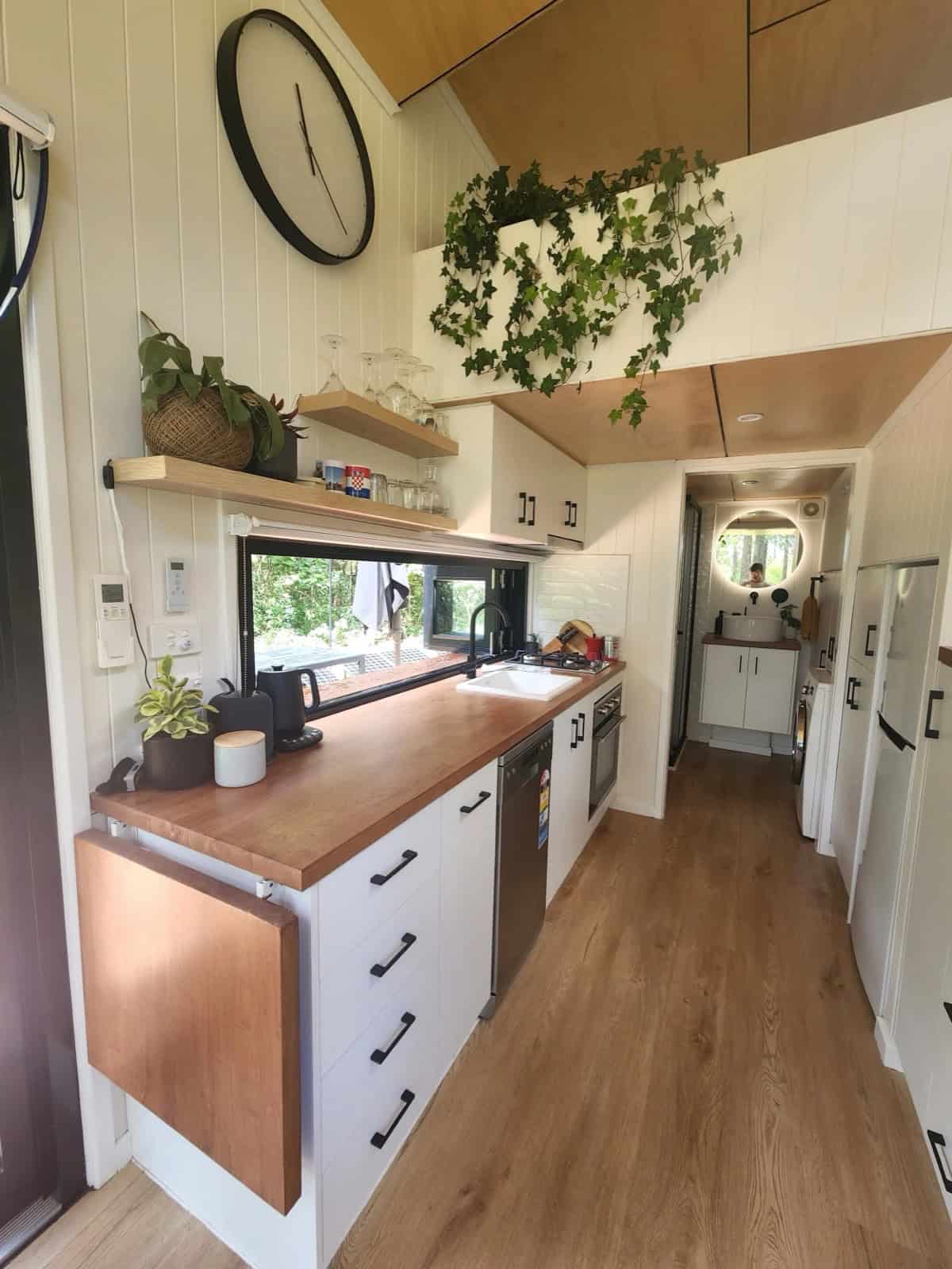 The Currumbin kitchen with timber benchtops, white cabinetry, a picture window over the sink, open shelving, and a fold-down timber bench