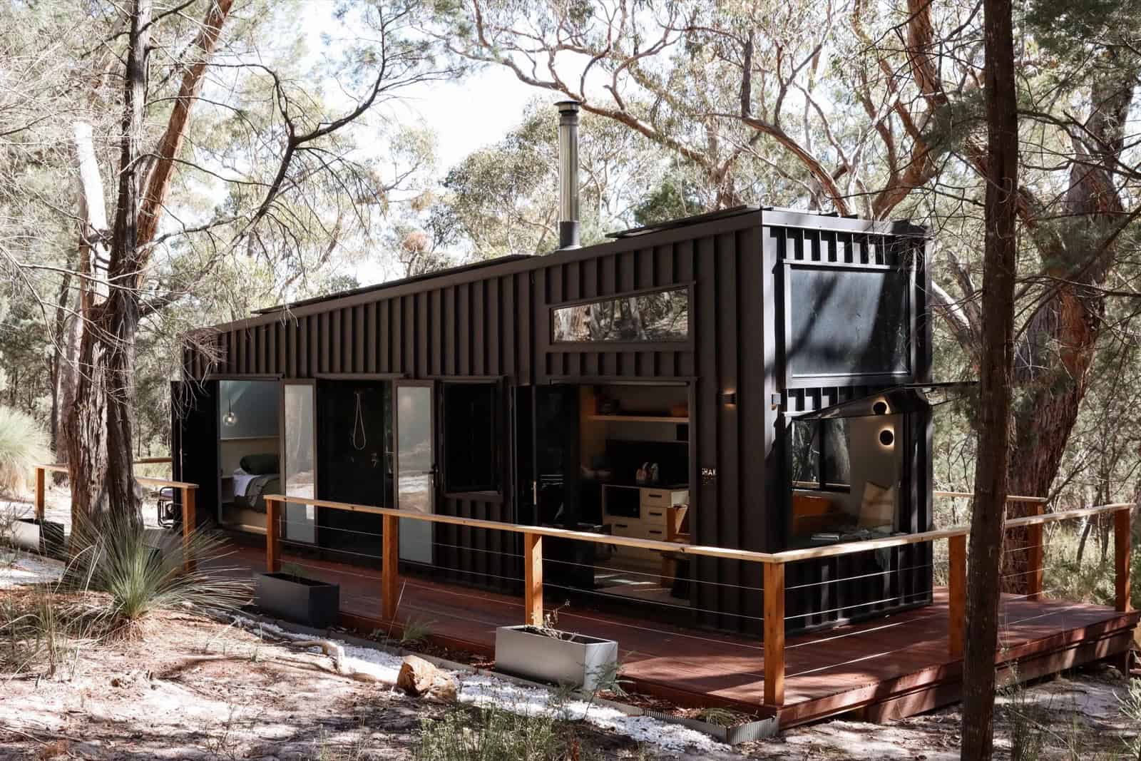 The SHAK seen from the deck with its glass doors open, dark cladding and timber-and-cable balustrade set against the surrounding bushland