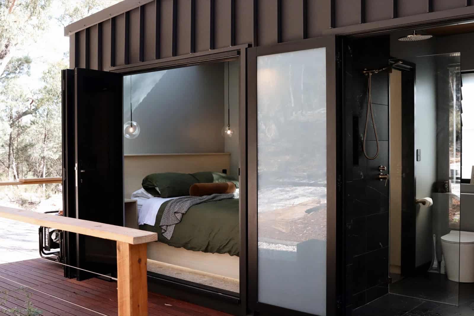 The SHAK with its bedroom and bathroom glass doors folded fully open onto the timber deck, connecting the interior to the surrounding bushland