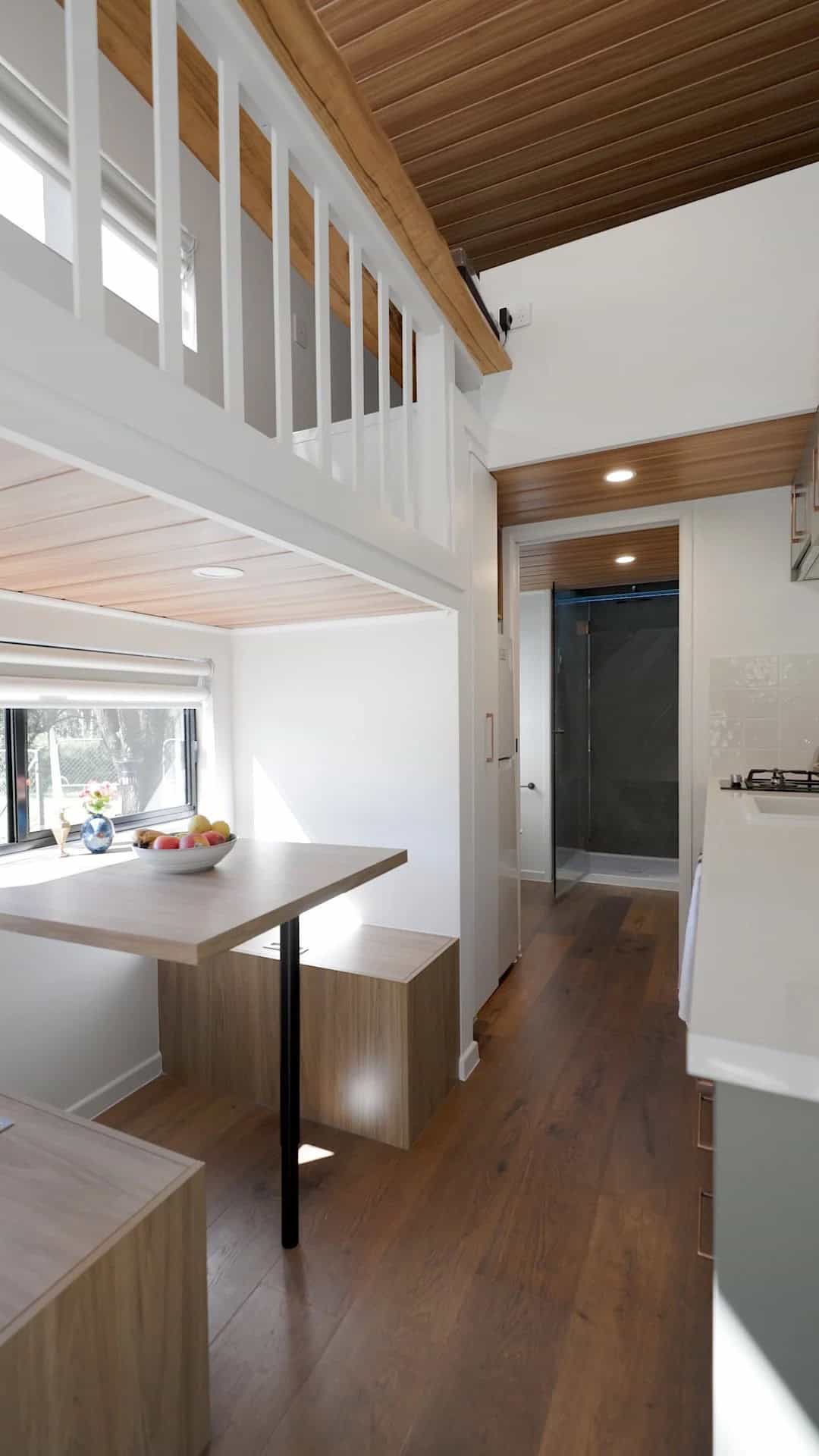 A built-in dining nook with a timber table and bench seating tucked beneath the Springbrook's corner stairway and loft, with the bathroom visible down the hall