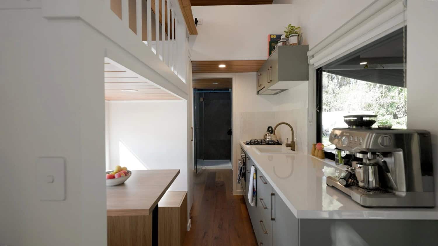 The Springbrook galley kitchen with sage-green cabinetry, brushed-copper handles, white stone benchtops, a brass tap, and a dining nook tucked beneath the corner stairway