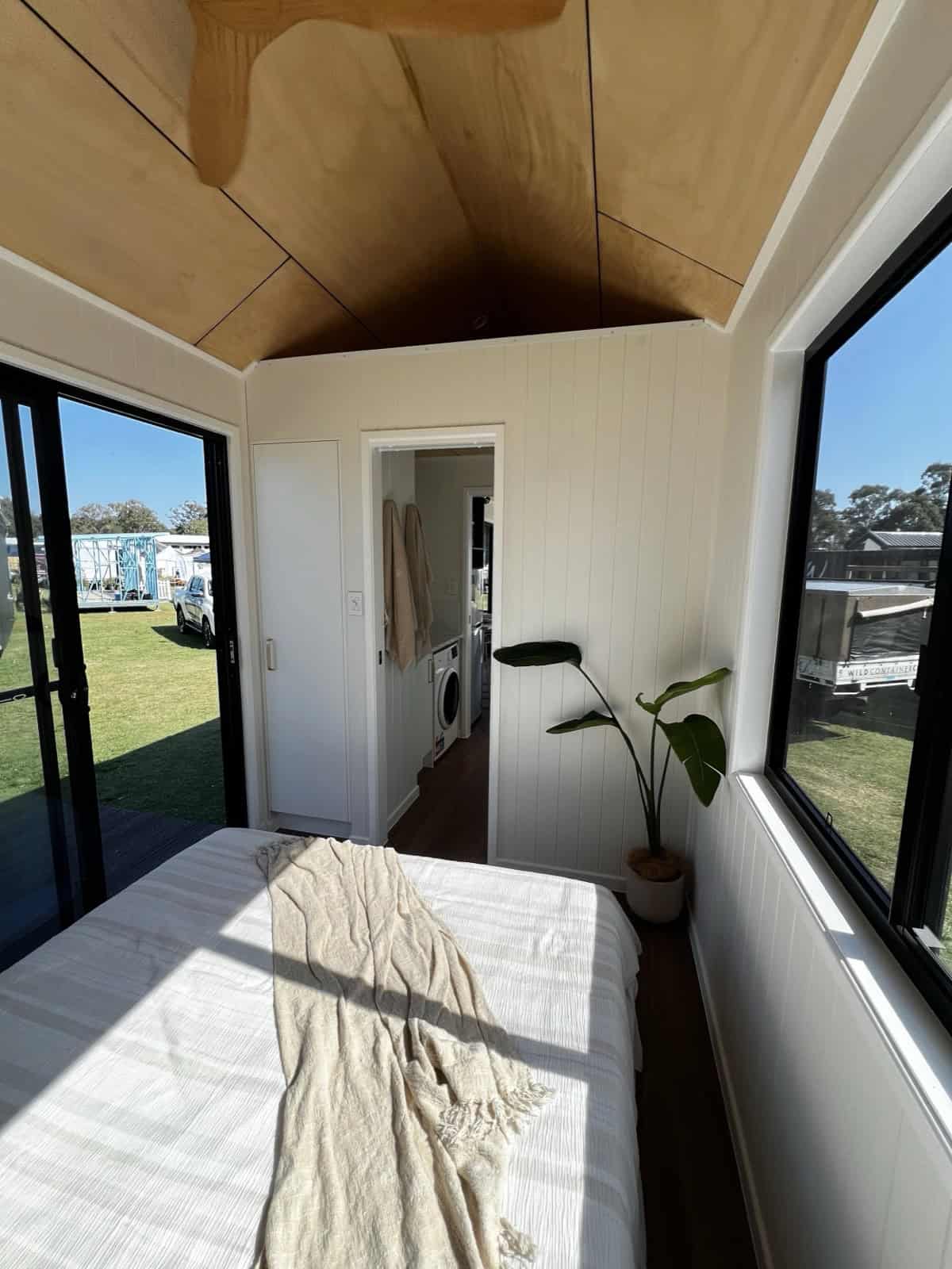 The ground-floor bedroom of the Tallebudgera with a queen bed, a vaulted timber ceiling, windows on two sides, a sliding glass door, and the ensuite visible through the doorway