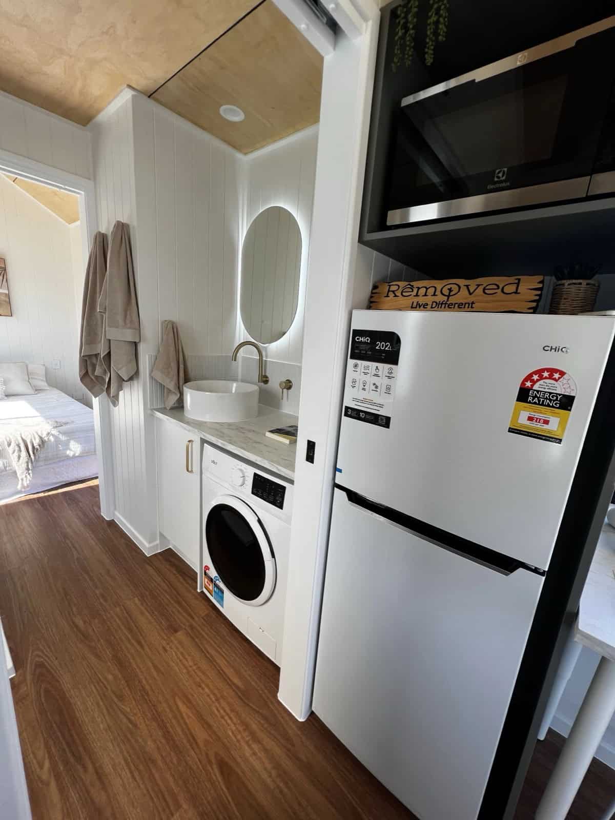 The Tallebudgera vanity with a round vessel sink and brass tap, a front-loading washing machine built in beneath the bench, and a tall fridge with an overhead microwave alongside
