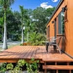 Compact tiny house with wooden deck and outdoor seating.