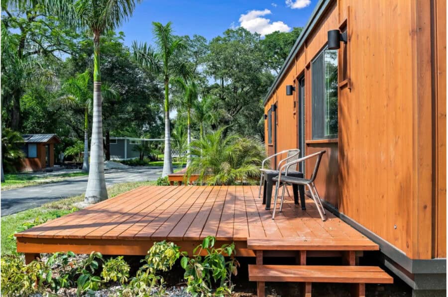 Compact tiny house with wooden deck and outdoor seating.