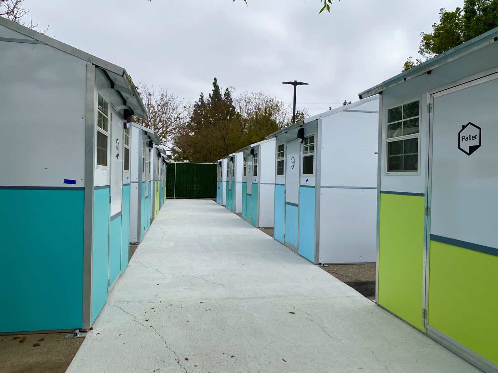 Teal and lime green Pallet tiny homes facing each other across a concrete walkway at Reseda tiny home village