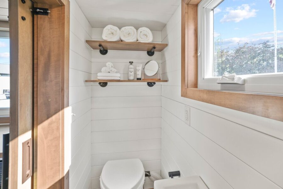 Bright tiny bathroom with white shiplap walls and natural wood accents.