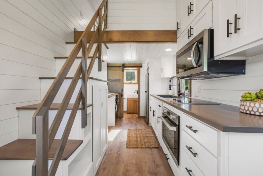Modern tiny home kitchen with white cabinets and wooden accents.