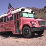 Vintage pink tiny house bus with American flag on a desert landscape.