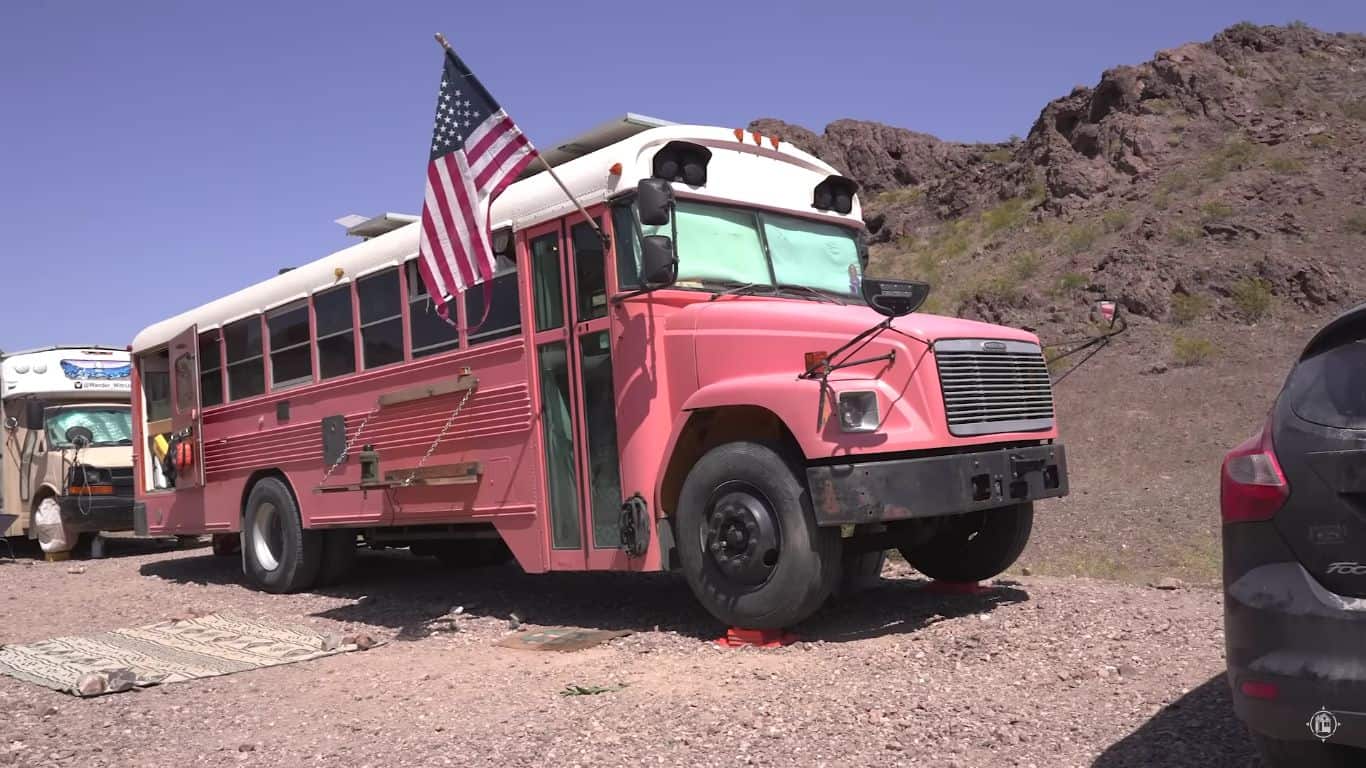 Vintage pink school bus converted into tiny home with American flag.