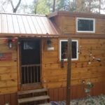 Cozy tiny house with loft and outdoor porch in a wooded setting.