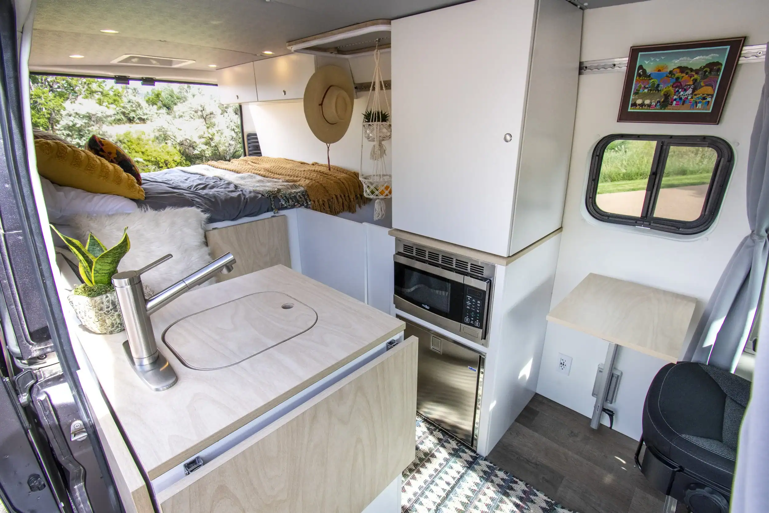 Interior of a tiny house showing a small kitchen, bed, and window view of nature.