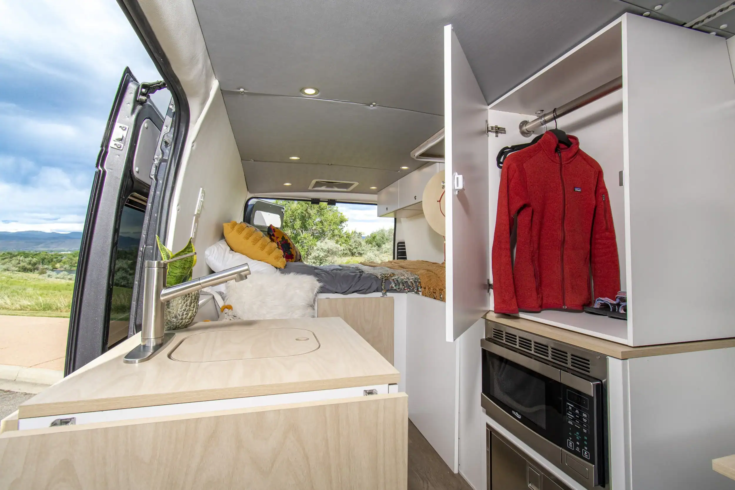 Compact tiny house interior featuring a bed, kitchen sink, and storage closet.