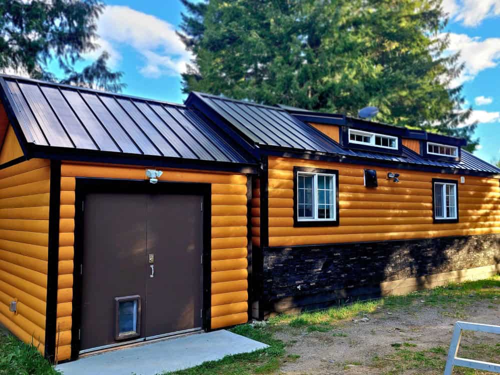 Side view of the Black Bear cottage showing log siding, dormer windows, stone skirting, and a dark metal roof