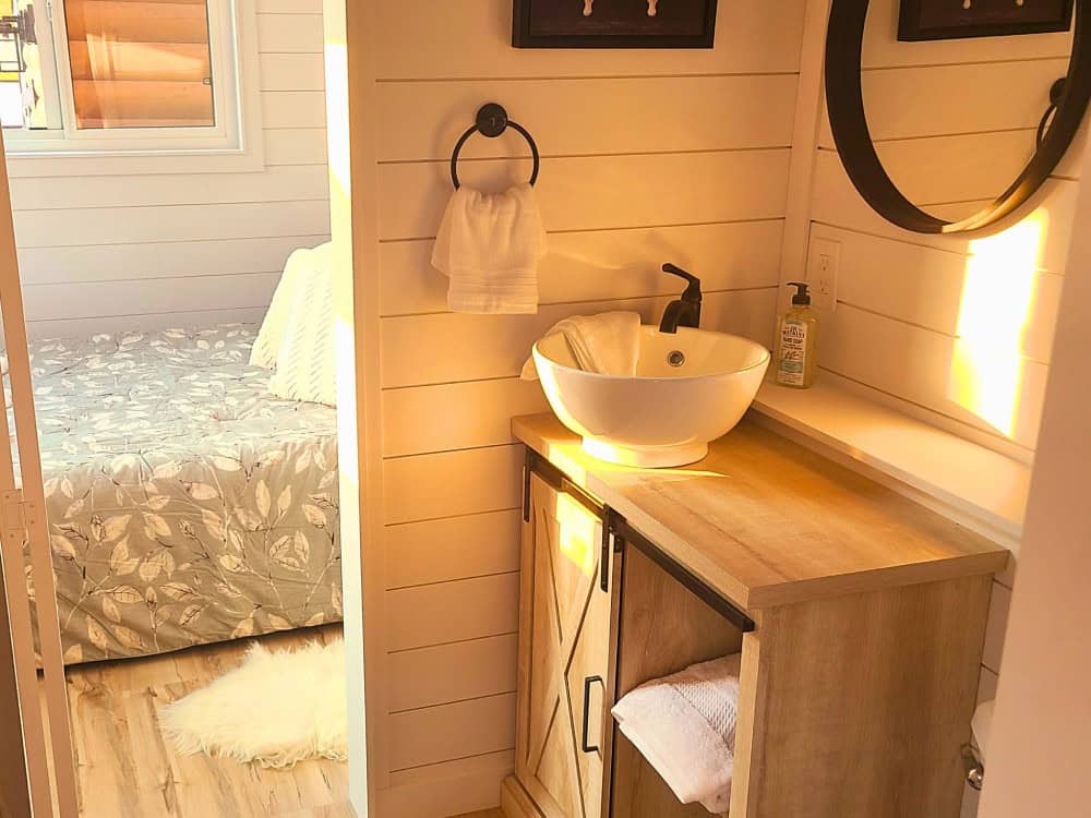 Cinnamon Bear bathroom vanity with a white vessel sink, round mirror, wood barn-door cabinet, and shiplap walls