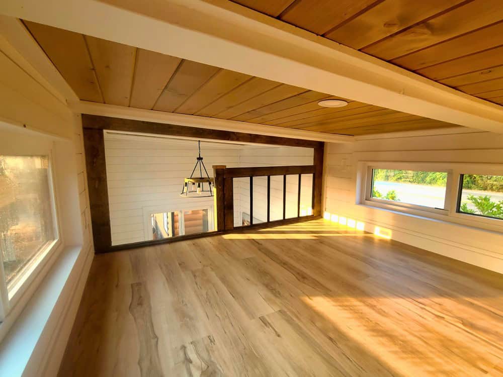 Elevated open-plan living level in the Cinnamon Bear framed by reclaimed timber posts and a slatted railing under a vaulted cedar ceiling