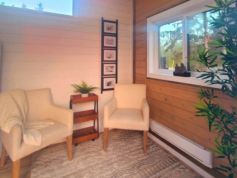 Cinnamon Bear sitting area with two cream armchairs, a cedar accent wall, a picture ladder, and a window