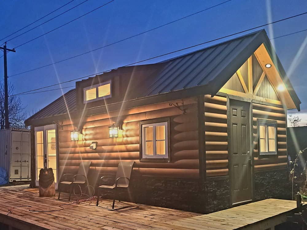 Rolling Bear Cub Bear solo retreat lodge glowing at dusk, a log cabin with a green metal roof, dormer, and deck