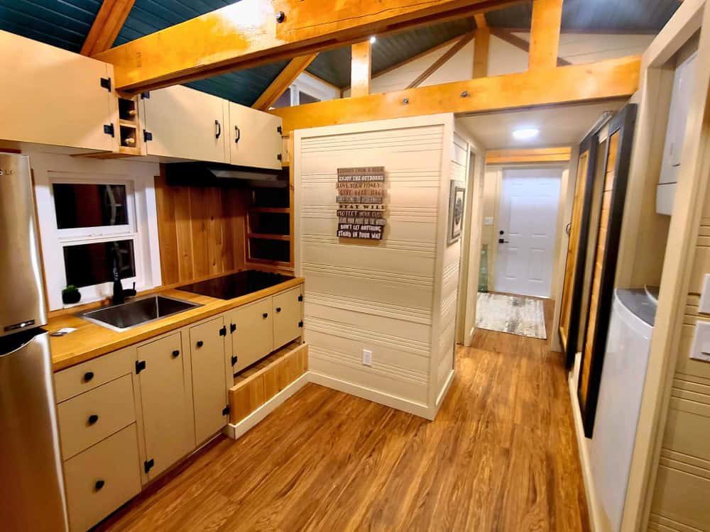 Cub Bear kitchen with butcher-block counters, cooktop, sink, refrigerator, and white cabinetry under a vaulted truss ceiling