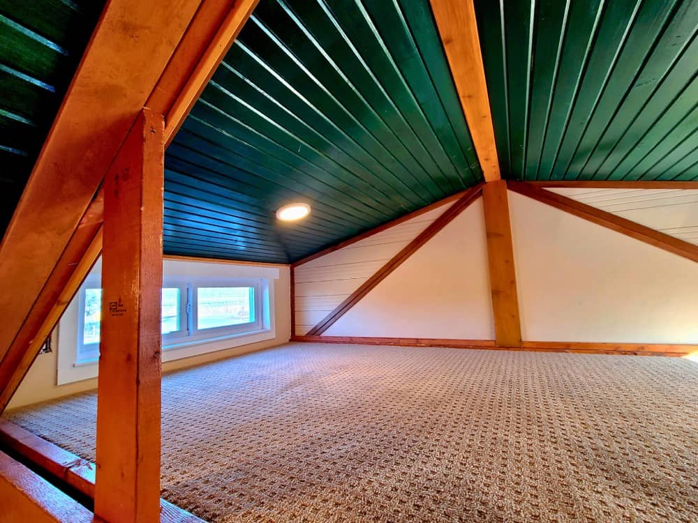 Carpeted sleeping loft in the Cub Bear with a green plank ceiling, exposed trusses, and a window
