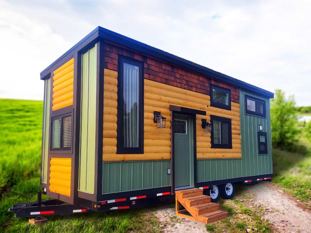 Rolling Bear Fraser Bear family lodge in a green meadow, with log siding, green and yellow accents, cedar-shake dormers, and a trailer chassis