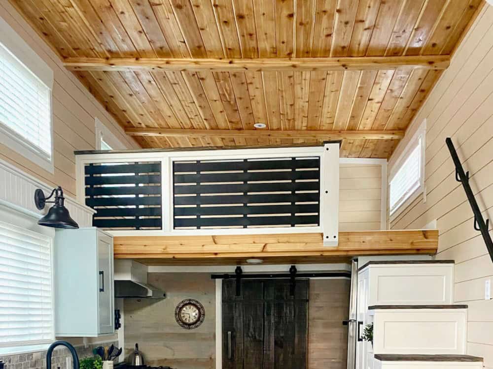 Fraser Bear kitchen beneath a vaulted cedar ceiling with a slatted loft railing, range hood, white cabinetry, and a reclaimed barn door