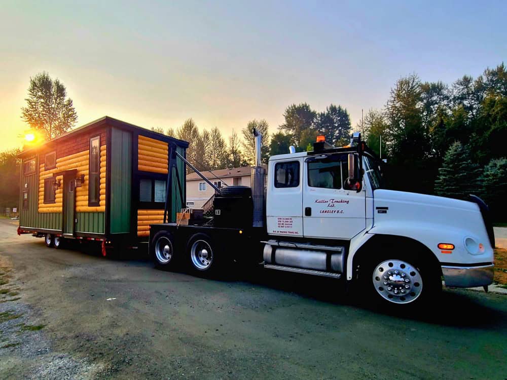 The Fraser Bear family lodge being hauled to its site on a trailer behind a semi truck at sunset