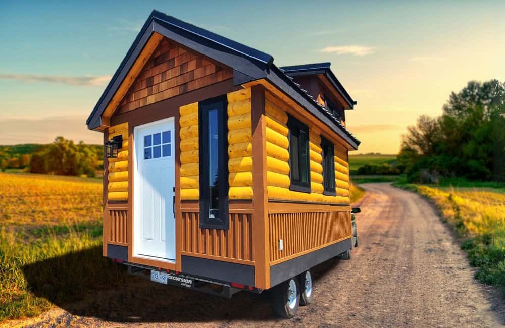 Rolling Bear Honeycomb Office Farmhand, a small log-cabin tiny house on wheels with a cedar-shake gable and white door, parked on a country lane at golden hour