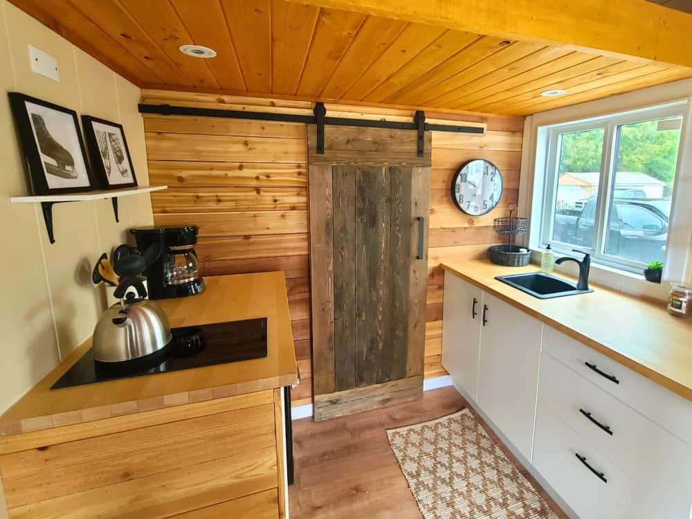 Honeycomb Office Farmhand kitchenette with butcher-block counters, a black sink, a cooktop, white cabinets, and a reclaimed-wood barn door