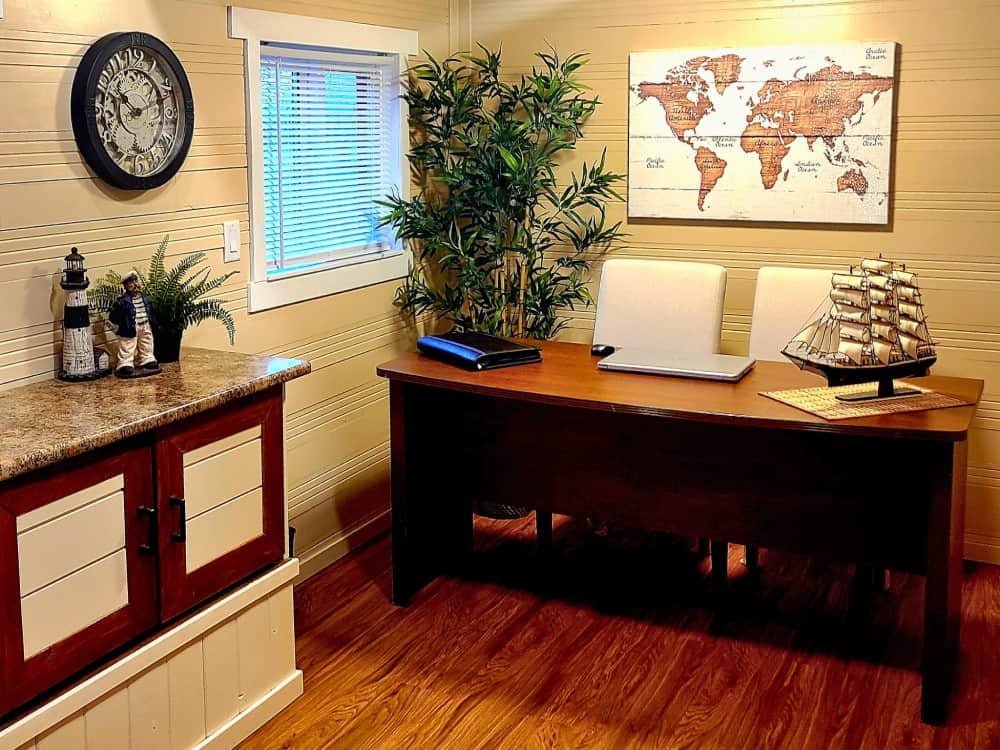 Interior office of the Honeycomb Mobile Office with a large wooden executive desk, laptop, world-map art, and a window