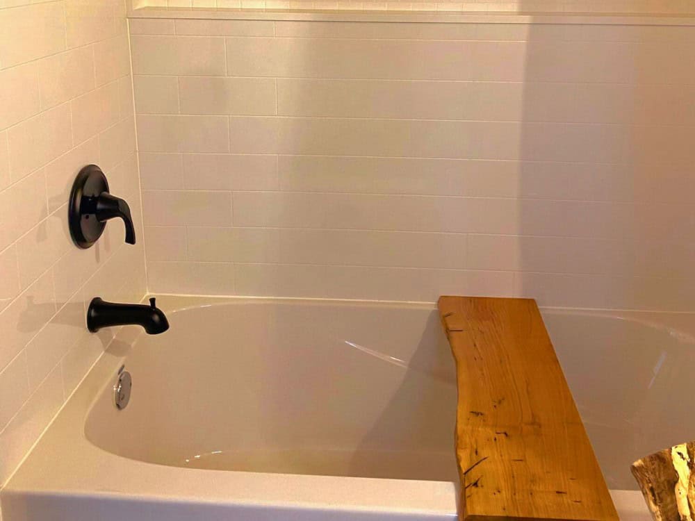 Full bathroom in the Koala Bear with a white soaking tub, tiled surround, and a live-edge wood bath shelf