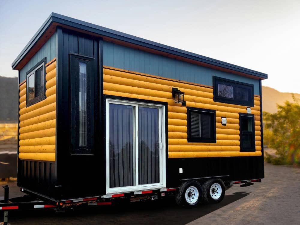 Rolling Bear Panda Bear solo retreat lodge with black board-and-batten, teal, and golden half-log siding, a sliding glass door, and a dual-axle trailer