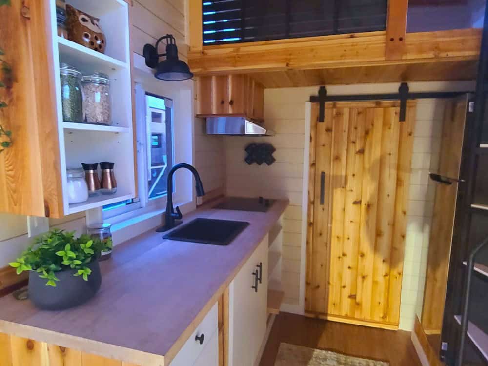 Panda Bear kitchenette with butcher-block counter, black sink, cooktop, open shelving, and a cedar barn door