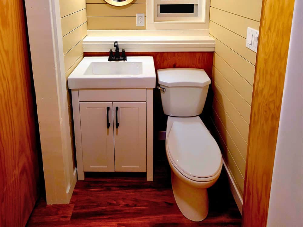 Full bathroom in the Salmon Bear with a white vanity, flush toilet, round mirror, and shiplap walls