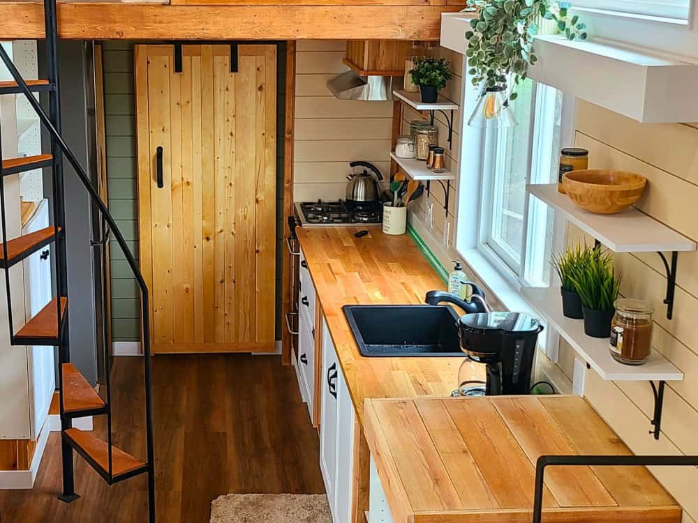 Skylar Bear galley kitchen with butcher-block counters, a gas cooktop, a black sink, open shelving, and a barn-door pantry beside a spiral staircase