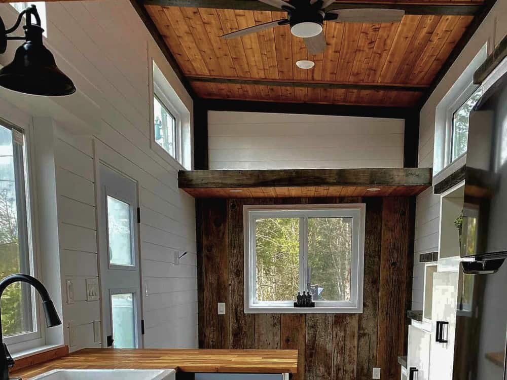 Vaulted cedar great room of the Spirit Bear with exposed reclaimed beams, a ceiling fan, white shiplap, and a reclaimed barn-wood accent wall around a window