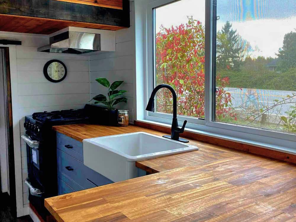Spirit Bear kitchen with a gas range, butcher-block counters, a white farmhouse apron sink under a window, and a stainless range hood