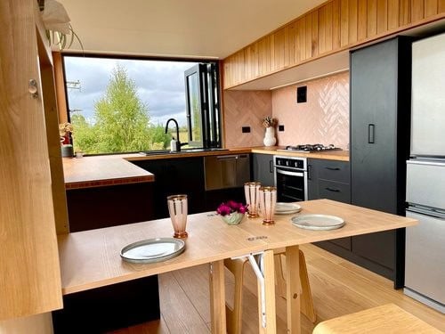 Modern tiny house kitchen with black cabinets, wooden accents, and a large window view.