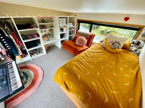 Cozy tiny house bedroom with large window, yellow bedding, and plush toys for a comfortable small sp.
