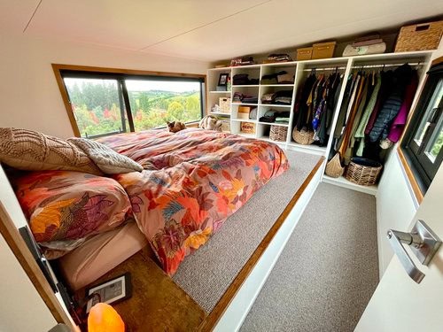 Compact tiny house bedroom with built-in closet and large window view.