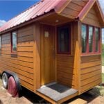 Rustic red tiny house with wooden exterior and small porch, perfect for minimalist living.